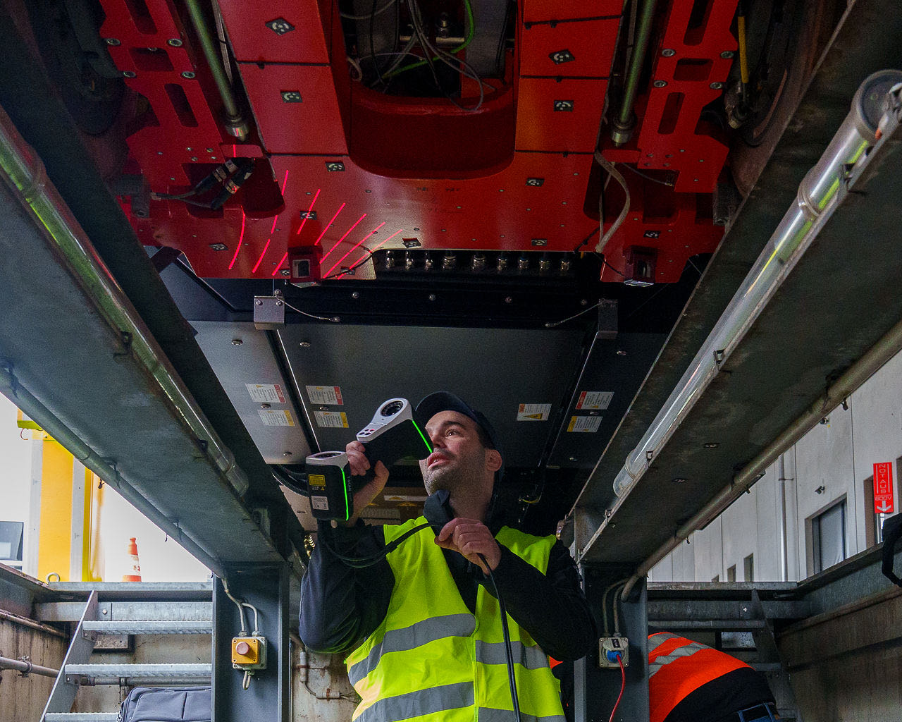 The active-steering bogie from an inspection pit, laser lines on it, a person in hi-vis scanning it with a handheld device.