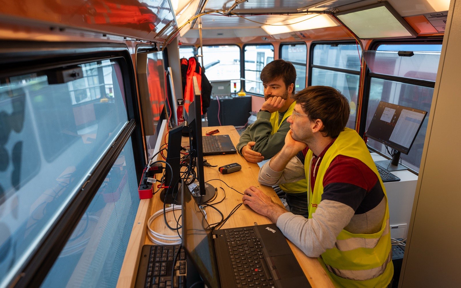 Inside the TX4 cab, two people at a desk with laptops and monitors.
