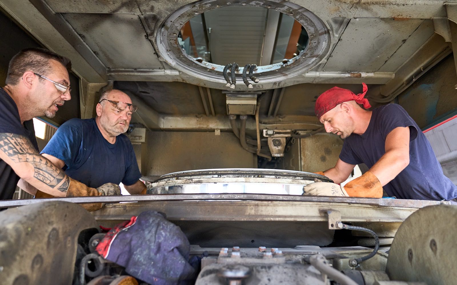 The underside of the TX4 test vehicle, a wheel and brake-disc assembly, three people working around it.