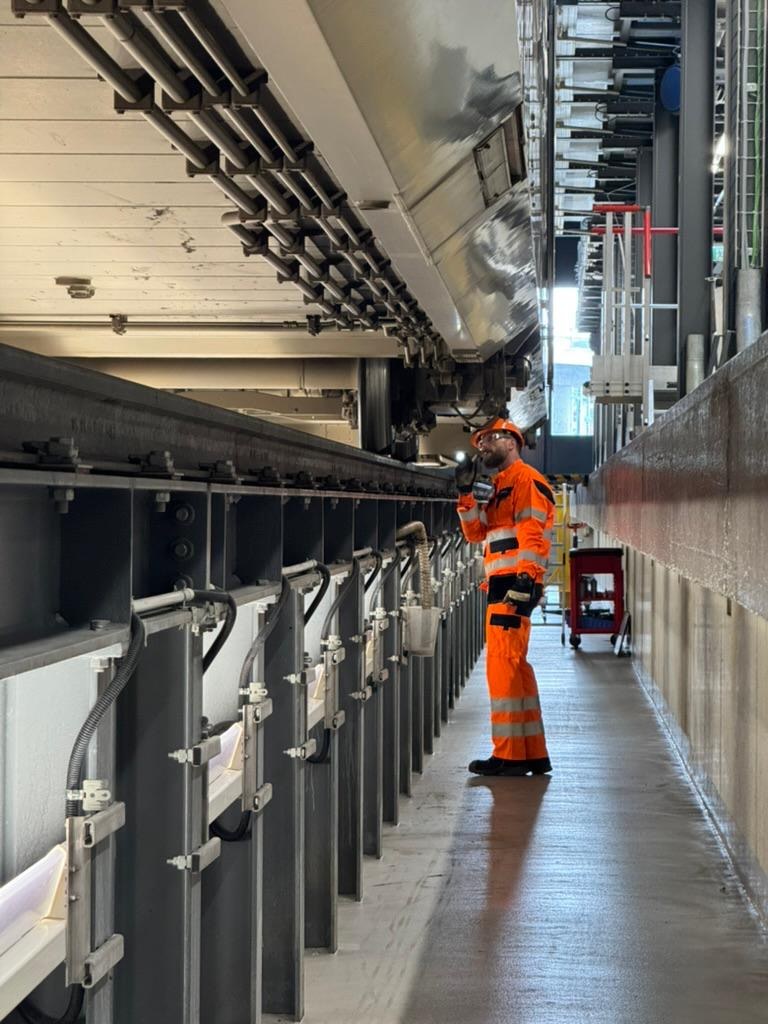 An inspector in orange hi-vis checking the underside of a rail vehicle from a depot pit.