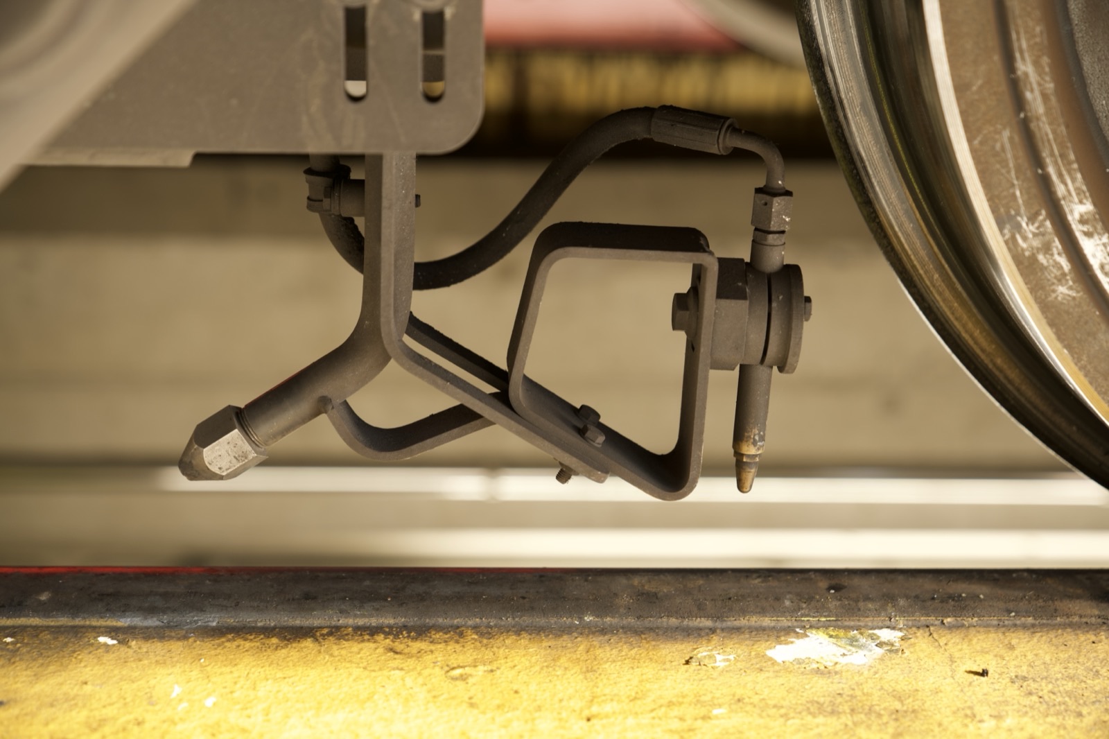 An onboard top-of-rail conditioning nozzle mounted beneath a rail vehicle bogie, close to the wheel.