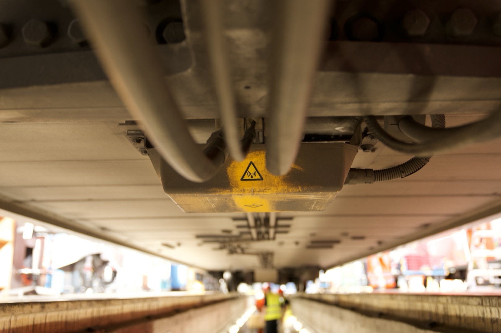 An electronics housing and cabling under a rail vehicle, photographed from the inspection pit during the SZU depot shoot.